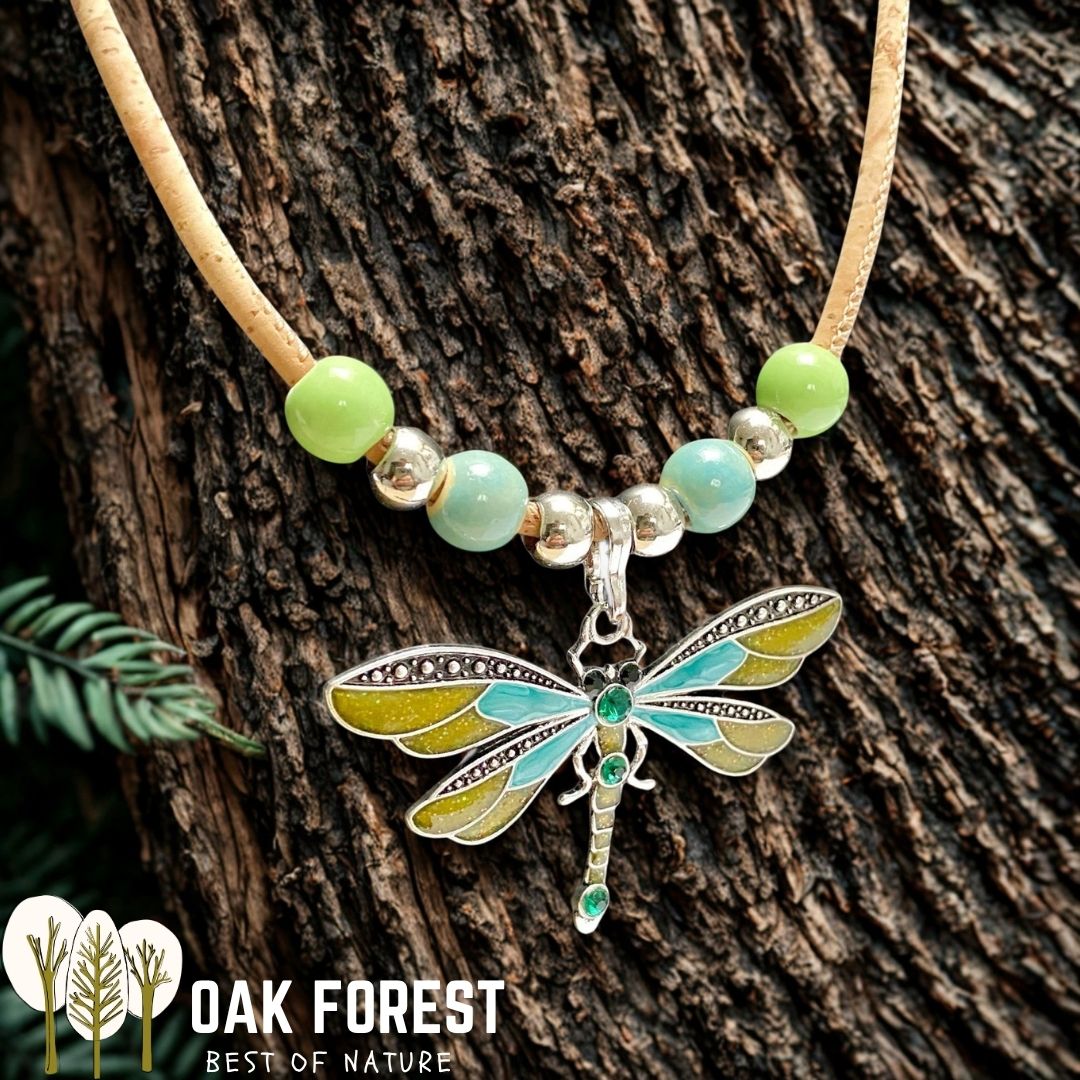 Collier en liège Libellule Color, pendentif libellule émaillé bleu et vert sur cordon liège avec perles vertes posé sur une écorce d'arbre